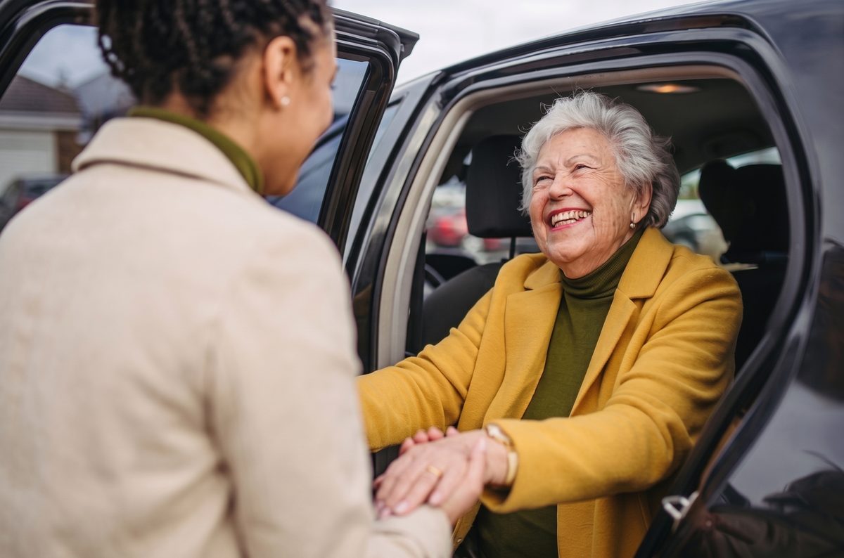 Una adulta mayor sonriente recibida al bajar del auto